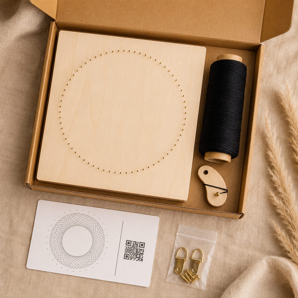 String-art kit flat-lay: pinned board, spool of black thread, thread holder, pattern card with QR code and hanging hardware in a kraft box