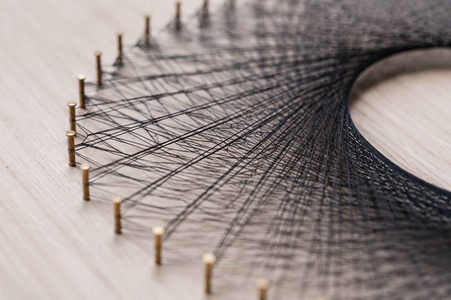 Macro close-up of fine black threads stretched between tiny brass pins on pale wood